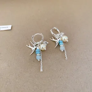 Vue détaillée de boucles d'oreilles créoles hirondelle en argent avec perles et glands.