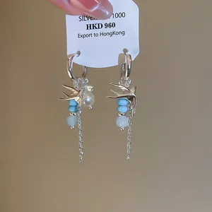 Gros plan de boucles d'oreilles hirondelles de style coréen avec perles et perles bleues.