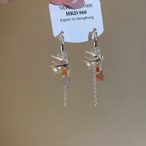 Détail de boucles d'oreilles hirondelle et perle avec chaînes en argent fines.