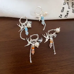 Détail de boucles d'oreilles en forme d'hirondelle avec perles et perles colorées.
