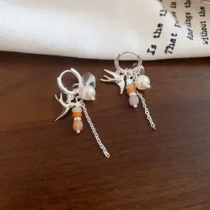 Détail macro des breloques hirondelle et perles blanches sur créoles élégantes en argent