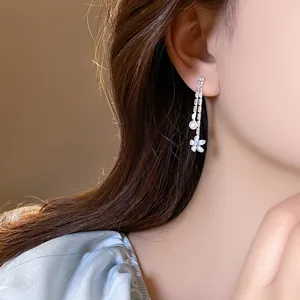 Detailed view of elegant light blue flower and pearl tassel earrings worn by a model