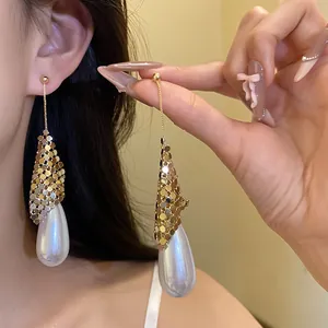 Close-up detail of elegant golden mesh and oversized teardrop pearl dangle earrings