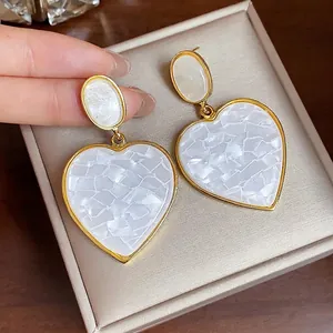 Elegant heart-shaped drop earrings with white mosaic resin and gold-tone trim.