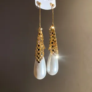 Detailed macro shot of elegant white teardrop pearl earrings with golden sequin mesh detail