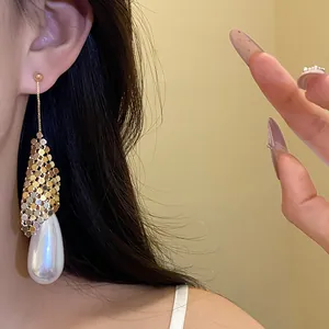 Close-up of elegant gold mesh earring with large pearlescent water drop pendant.