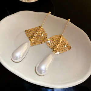Elegant detailed view of golden mesh and white teardrop pearl earrings on a dish
