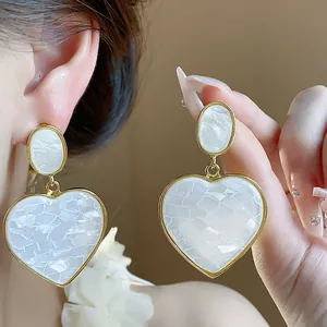 Close-up detail of elegant white resin heart drop earrings with gold metal frame.