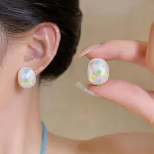 Detalle de pendientes de botón ovales mate con lunares de colores en oreja y mano