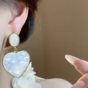 Detail shot of elegant heart-shaped white resin earrings with polished gold-tone metal trim
