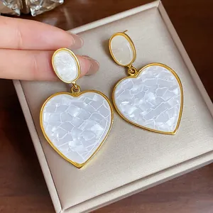 Close-up of white shell-textured resin heart drop earrings with an elegant gold finish.