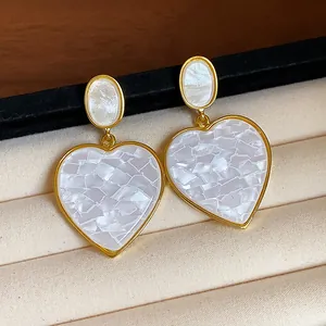 Close-up of gold heart earrings with white mosaic resin texture in a jewelry box