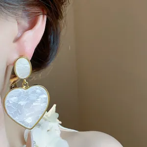 Close-up view of elegant white marbled resin heart drop earrings with a gold-tone border.