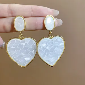 Detailed macro view of gold-trimmed white heart earrings with mosaic resin texture