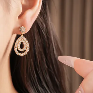 Detailansicht eines goldenen Tropfenohrrings mit funkelnden Zirkoniasteinen am Modellohr.