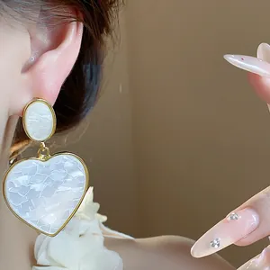 Detail showing large white resin heart pendant earring with elegant gold-tone framing
