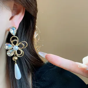 Close-up detail of an elegant gold-plated crystal flower earring with a pearl drop on a model.
