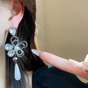 Close-up detail of luxurious floral crystal earrings with a white teardrop pendant