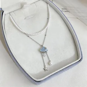 Close-up of a double-layered necklace with pearl beads and blue cloud charm in a jewelry box.