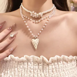 Detail shot of layered pearl necklace featuring flower accents and a resin heart pendant.