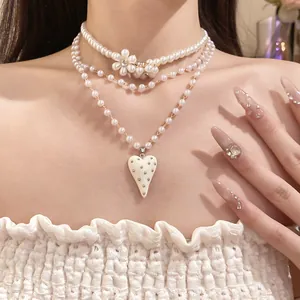 Close-up of three-layer pearl necklace with flower and studded resin heart pendant
