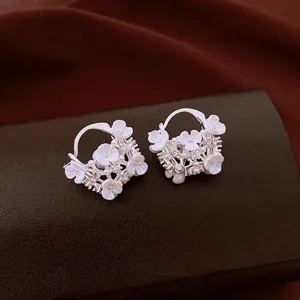 Elegant silver earrings with white flowers, pearls, and crystals on dark leather