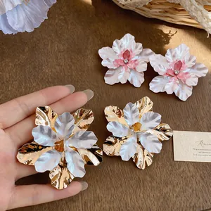 Detail view of oversized gold and white metal flower earrings with enamel finish