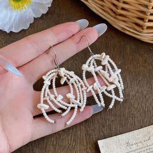 Close-up detail of bohemian style cream shell bead tassel drop earrings held in hand