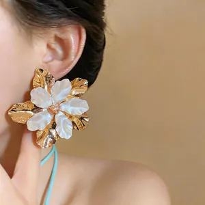 Close-up detail of elegant gold metal and pearlescent white flower stud earrings on a model