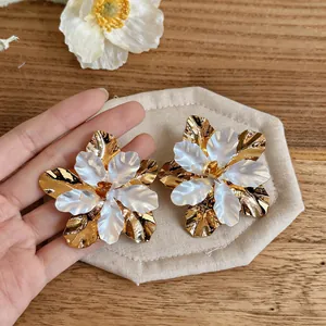 Detailed view of large gold and white metallic flower earrings with enamel petals.