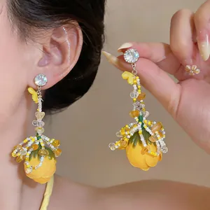 Close-up of elegant yellow floral drop earrings with rhinestone studs and bead fringes