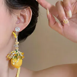 Detailed view of yellow floral bud tassel earrings with rhinestone stud on model