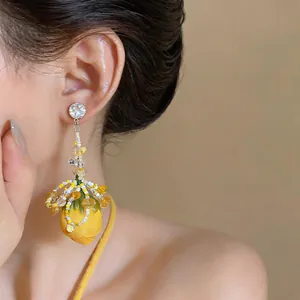 Close-up of exaggerated yellow flower bud drop earrings with beaded tassel design