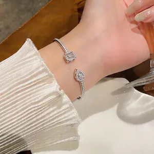 Elegant silver-tone open bangle with square and pear zircon stones on woman's wrist.