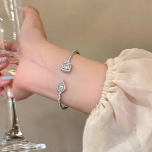 Elegant silver-toned open bangle featuring square and teardrop zircon stones on wrist