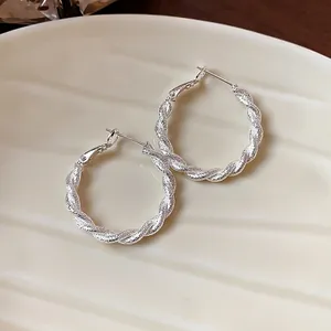 Dettaglio di orecchini a cerchio ritorti in argento dal design minimalista e satinato