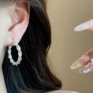 Dettaglio di un orecchino a cerchio ritorto in argento indossato, stile elegante.