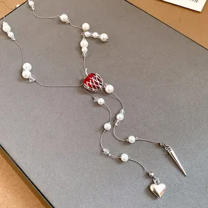 Elegant long pearl necklace featuring a red apple pendant with silver heart and spike charms.