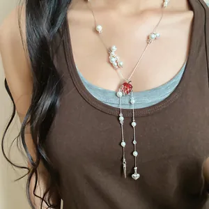 Detail shot of long necklace with pearls and red heart pendant worn on model.