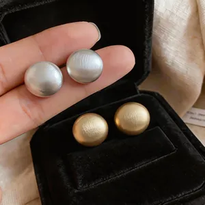 Dettaglio macro che mostra la texture spazzolata degli orecchini a lobo tondi oro e argento