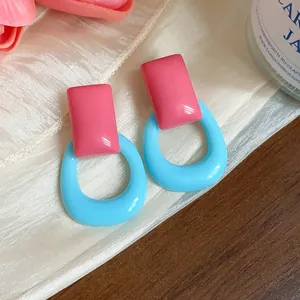 Close-up detail of pink rectangular and light blue hollow resin geometric earrings.