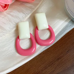 Close-up of pink and cream geometric resin hoop earrings on an elegant silk background