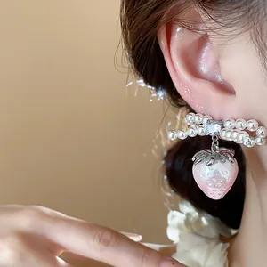 Detailed macro view of an elegant pink strawberry and pearl bow earring worn on ear