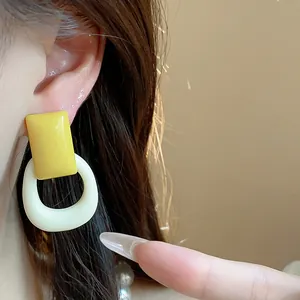 Close-up of vibrant yellow rectangular and white oval resin drop earrings shown on ear.