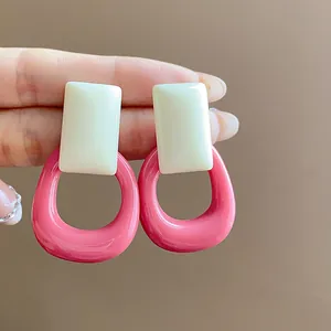 Close-up detail of pink and cream white resin hollow square stud earrings held by hand