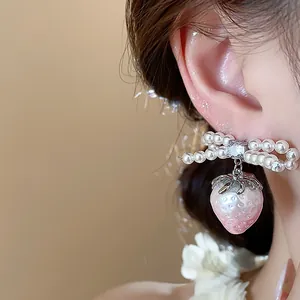 Detailed macro view of an elegant pink strawberry pearl bow stud earring on ear