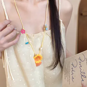 Detailed view of a yellow cord necklace with colorful flower and seashell charms on a model.