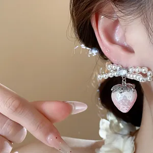 Close-up detail of delicate bowknot strawberry pearl earrings worn on an ear.