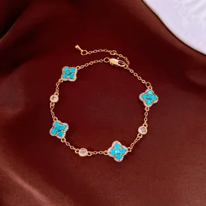 Close-up of a gold bracelet with turquoise four-leaf clover charms on brown fabric