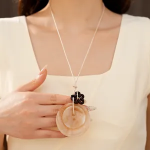Détail d'un collier avec pendentif circulaire en acrylique et fleur noire sur cordon beige